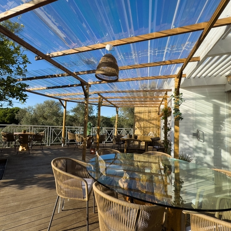 Aménagement terrasse moderne avec pergola et mobilier bois Terrasse en bois avec mobilier de jardin, table en verre et pergola transparente sous un ciel bleu ensoleillé.