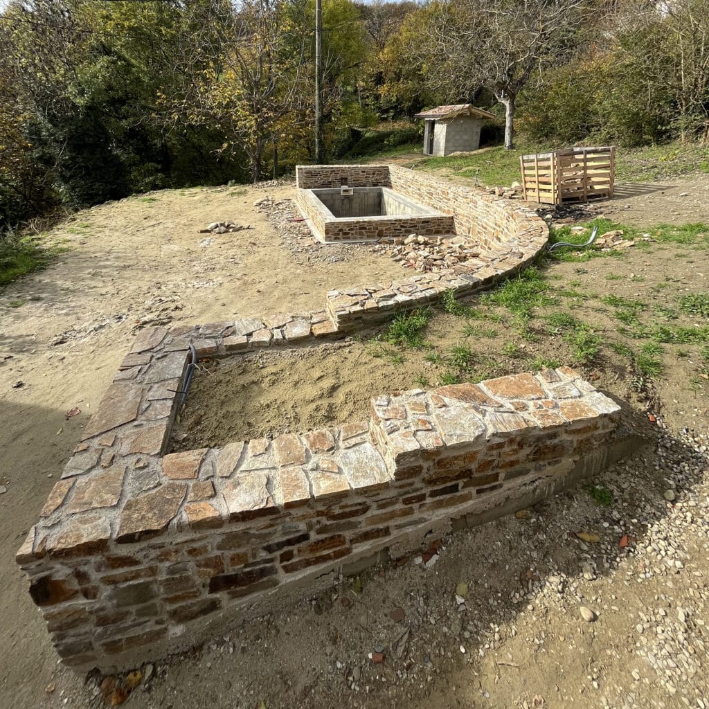 Aménagement paysager avec murs en pierre naturelle et bassin rectangulaire en cours de construction dans un jardin.