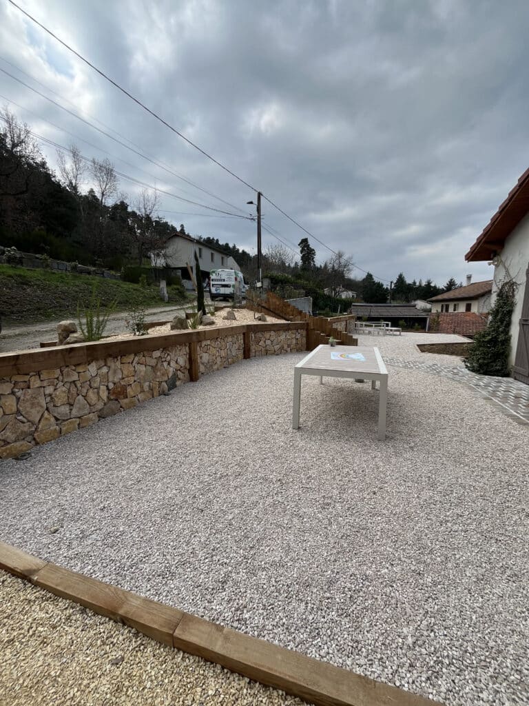 Terrasse en gravier blanc avec table de jardin et murets en pierre naturelle et bois.